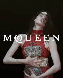 Model in red lace dress holding multiple embellished knuckle clutches against a dark background with white MCQUEEN text
