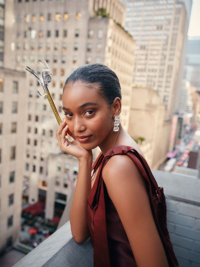 Elegant portrait of a woman in a brown dress on a rooftop with a cityscape background, showcasing fashion and urban lifestyle.