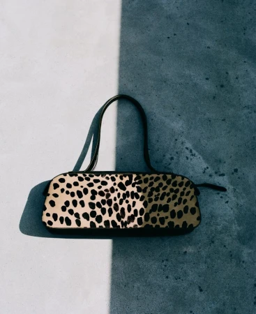 Overhead studio shot of a stylish handbag with black spots and a brown handle, casting a shadow on a split grey and white background.