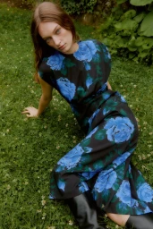 Model seated on a lush green lawn wearing a dark blue floral print dress by Lela Rose for Fall 2025.