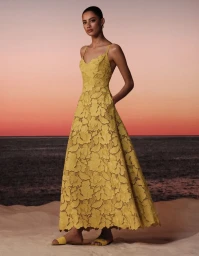 Model in a yellow lace dress standing on a sandy beach against a sunset sky