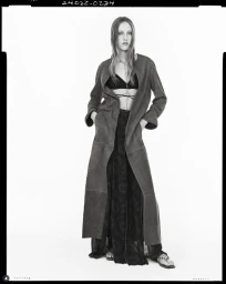 Monochrome fashion editorial image of a female model in a long coat standing against a white seamless background for Zara studio SS25.