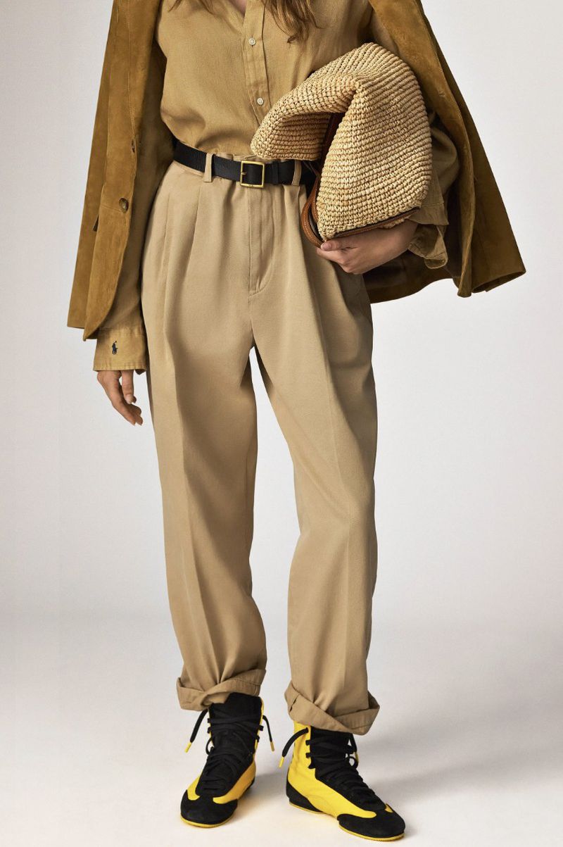 Fashionable adult woman posing in a studio setting, wearing brown pants and jacket with yellow and black sneakers.
