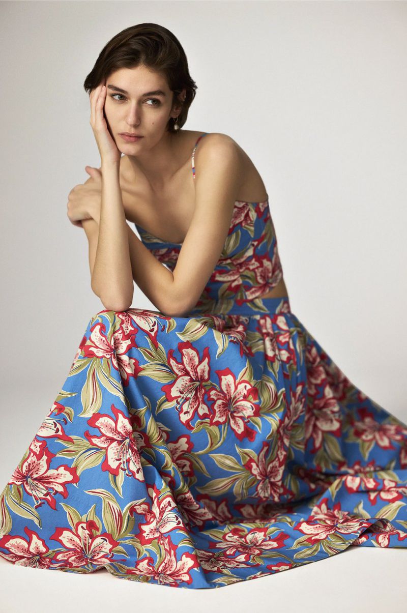 Woman in floral two-piece set poses in a studio, showcasing fashion and beauty with natural lighting, against a neutral backdrop.