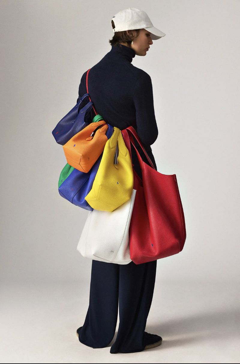 Fashion shot featuring a person wearing a cap and carrying multiple colorful tote bags against a neutral studio backdrop.