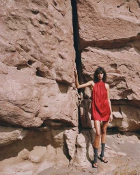 Model Mica Argañaraz in a sleeveless red mini dress posing against large desert rock formations for Mango.