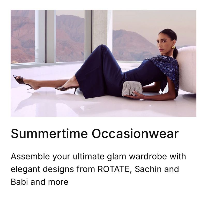 Elegant adult female model poses in a navy dress and heels, lying on a white surface with a silver clutch in a fashion setting.