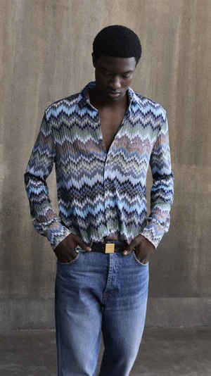 Model wearing Missoni zig-zag patterned shirt and blue jeans against a textured concrete wall.