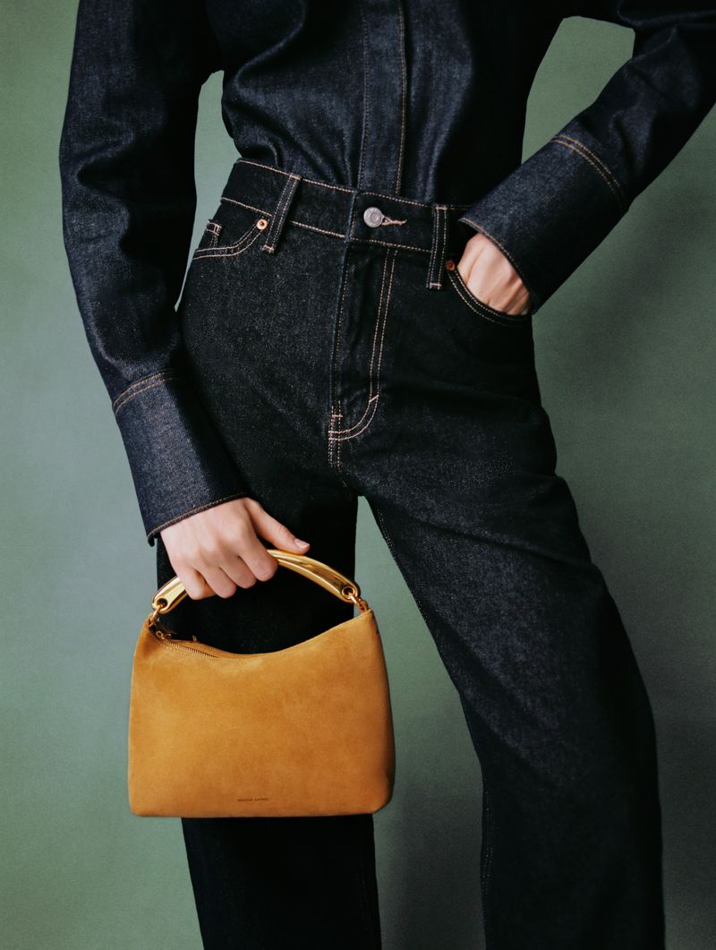A person wearing a denim shirt and jeans holds a yellow handbag in a medium studio shot, highlighting fashion and style.