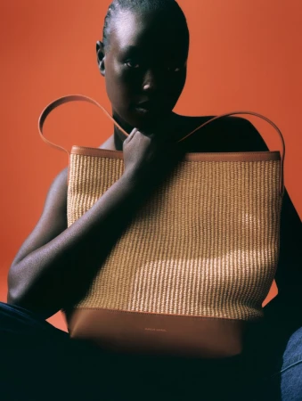 Dark-skinned woman poses with a woven straw tote bag against a red background in a studio shot emphasizing fashion and texture.