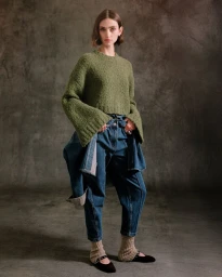 Model wearing an olive green cropped knit sweater and layered denim jeans against a textured backdrop for 3.1 Phillip Lim.