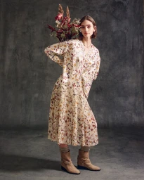 Model wearing a cream floral print midi dress and tan suede boots holding dried flowers against a dark textured backdrop.