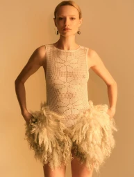 Model Maya Stepper posing in a cream crochet bodysuit with textured shearling hips against a warm backdrop.
