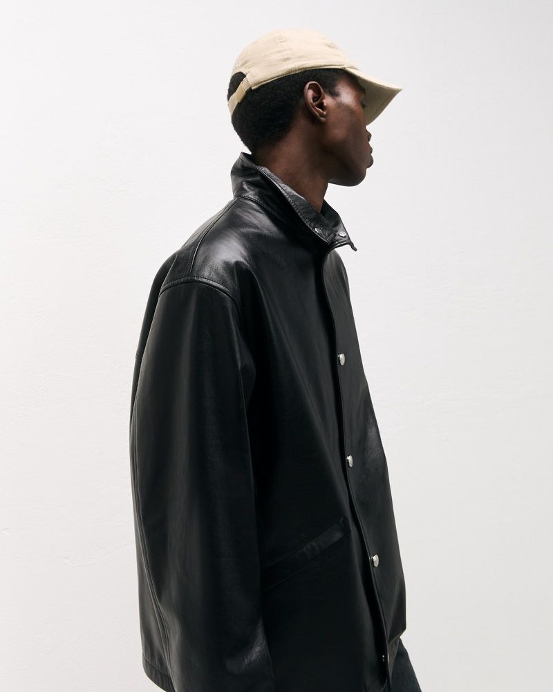 Profile shot of an African American man wearing a leather jacket and baseball cap against a neutral backdrop in a studio environment.