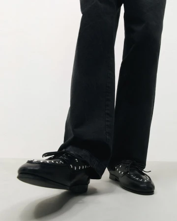 Black leather dress shoes with silver metal eyelets. The shoes are worn with dark trousers. The image is shot in a photo studio.