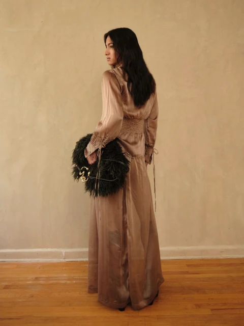A brunette woman in a satin dress poses with a feather boa against a neutral backdrop, looking over her shoulder with a subtle smile.
