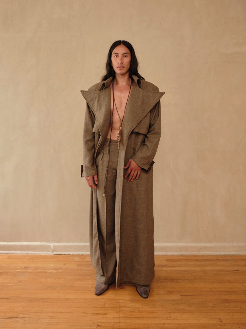 A man in a stylish brown trench coat and pants stands against a neutral backdrop, showcasing a fashionable, confident, and sophisticated look.