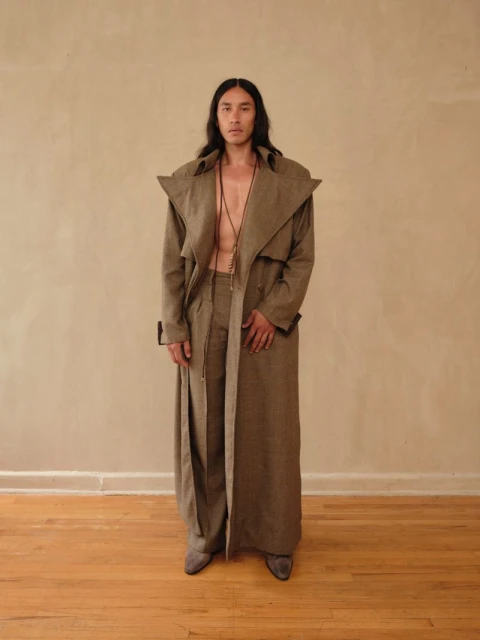 A man in a stylish brown trench coat and pants stands against a neutral backdrop, showcasing a fashionable, confident, and sophisticated look.