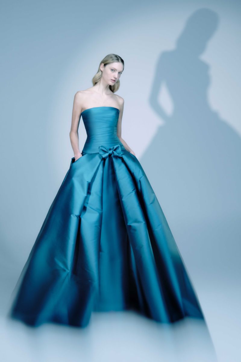 Fashion model in a teal strapless ballgown poses in a studio with a silhouette shadow, creating an elegant and timeless visual narrative.