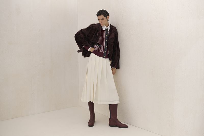Fashion shot of a woman in a fur jacket, striped top, and white skirt, accessorized with knee-high boots, posing against a neutral backdrop.