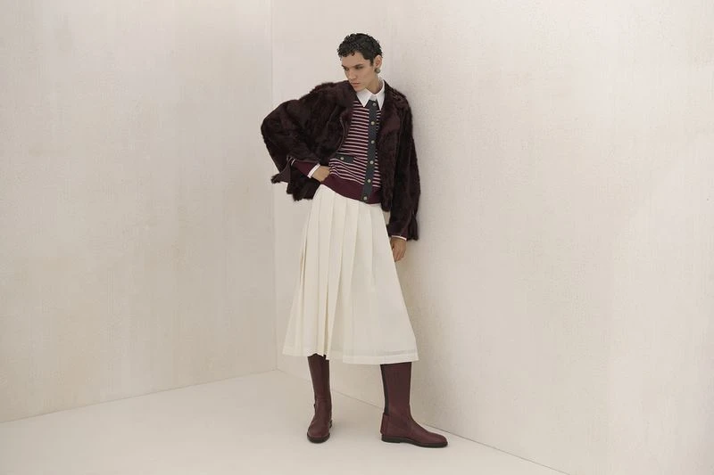 Fashion shot of a woman in a fur jacket, striped top, and white skirt, accessorized with knee-high boots, posing against a neutral backdrop.