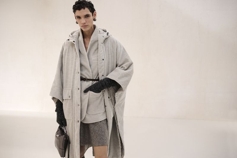 Fashionable woman in grey coat and skirt holding purse in studio, stylish contemporary outfit. Cool-toned lighting, elegant.