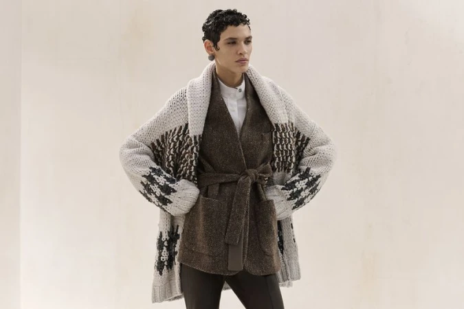 Female model wearing a brown belted jacket and patterned knit cardigan in a fashion editorial studio shot.