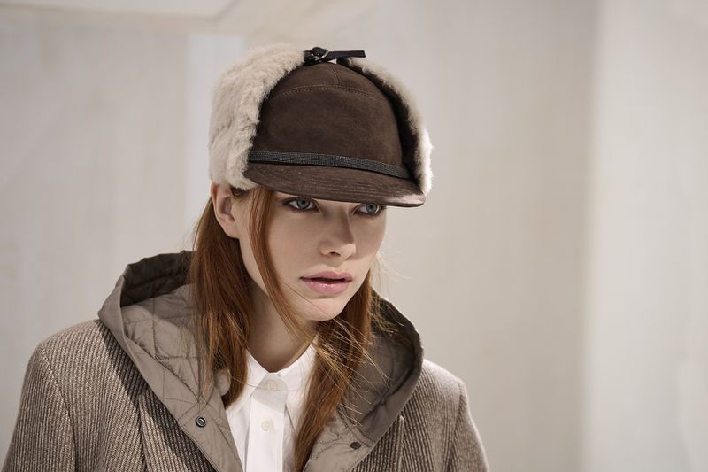 Headshot of a redhead woman wearing a brown hat with fur trim and a coat. The model is indoors, posing against a plain background.
