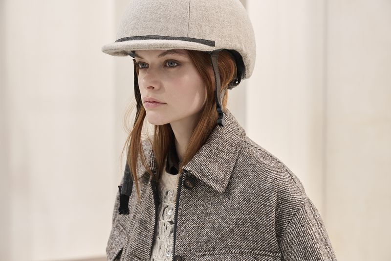 Woman poses in tweed jacket and riding helmet. Head and shoulders shot against neutral background, looking left.