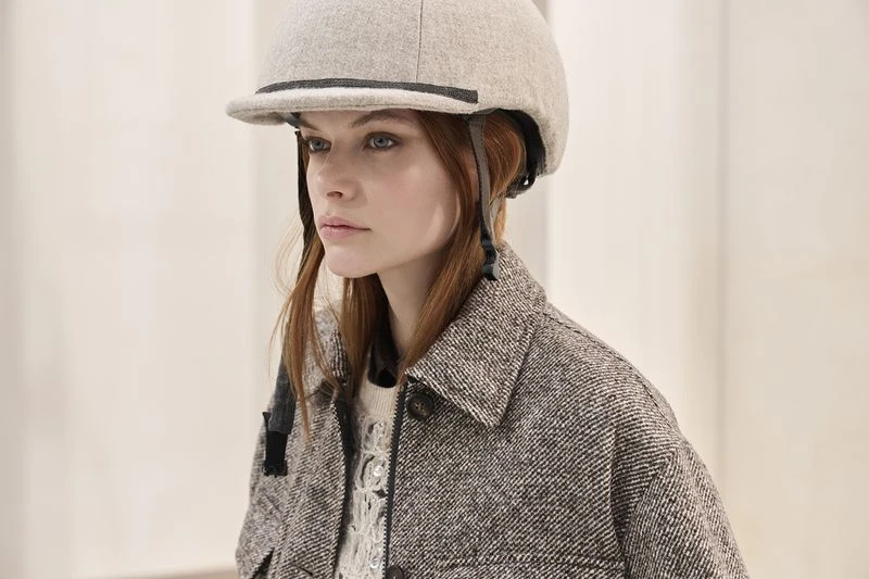 Woman poses in tweed jacket and riding helmet. Head and shoulders shot against neutral background, looking left.
