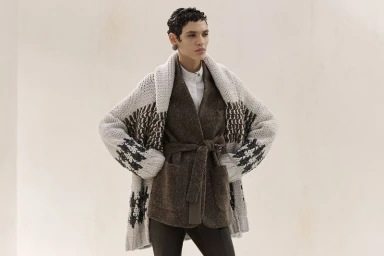 Model wearing a chunky patterned cardigan and brown belted coat against a neutral seamless background