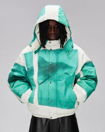 An adult in a hooded puffer jacket with a white and teal abstract print poses in front of a light gray background.