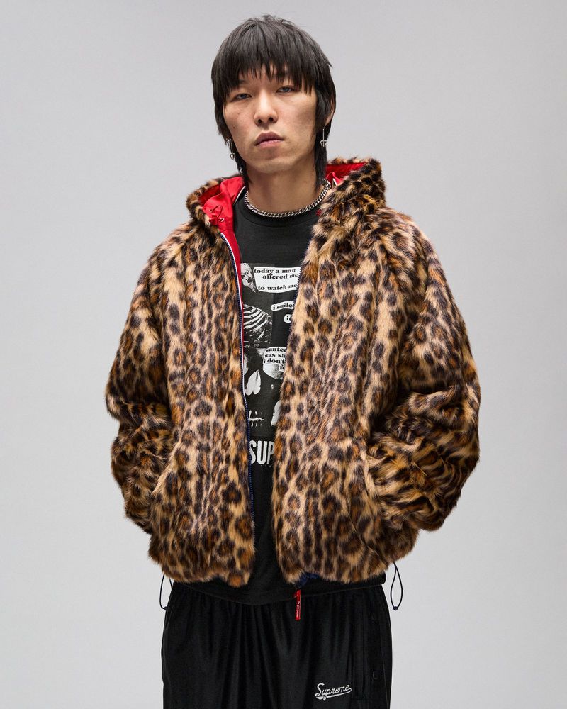 Asian man in a leopard print faux fur hooded jacket over a black graphic tee shirt, standing against a light gray studio backdrop.