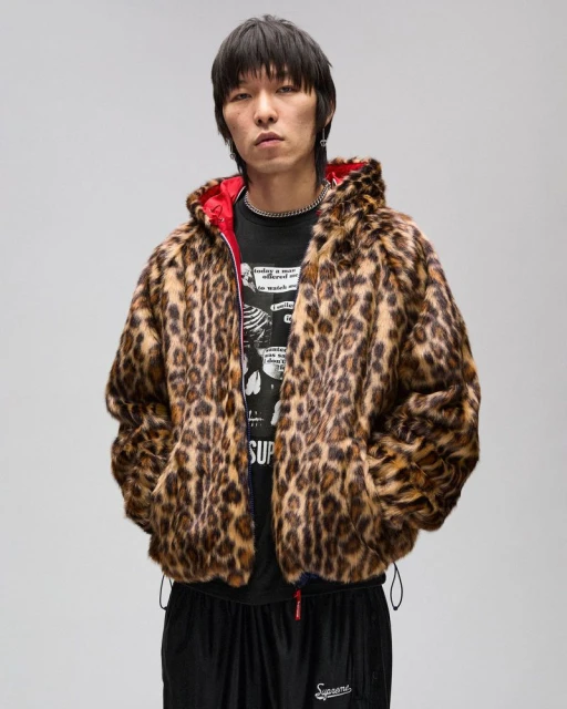 Asian man in a leopard print faux fur hooded jacket over a black graphic tee shirt, standing against a light gray studio backdrop.