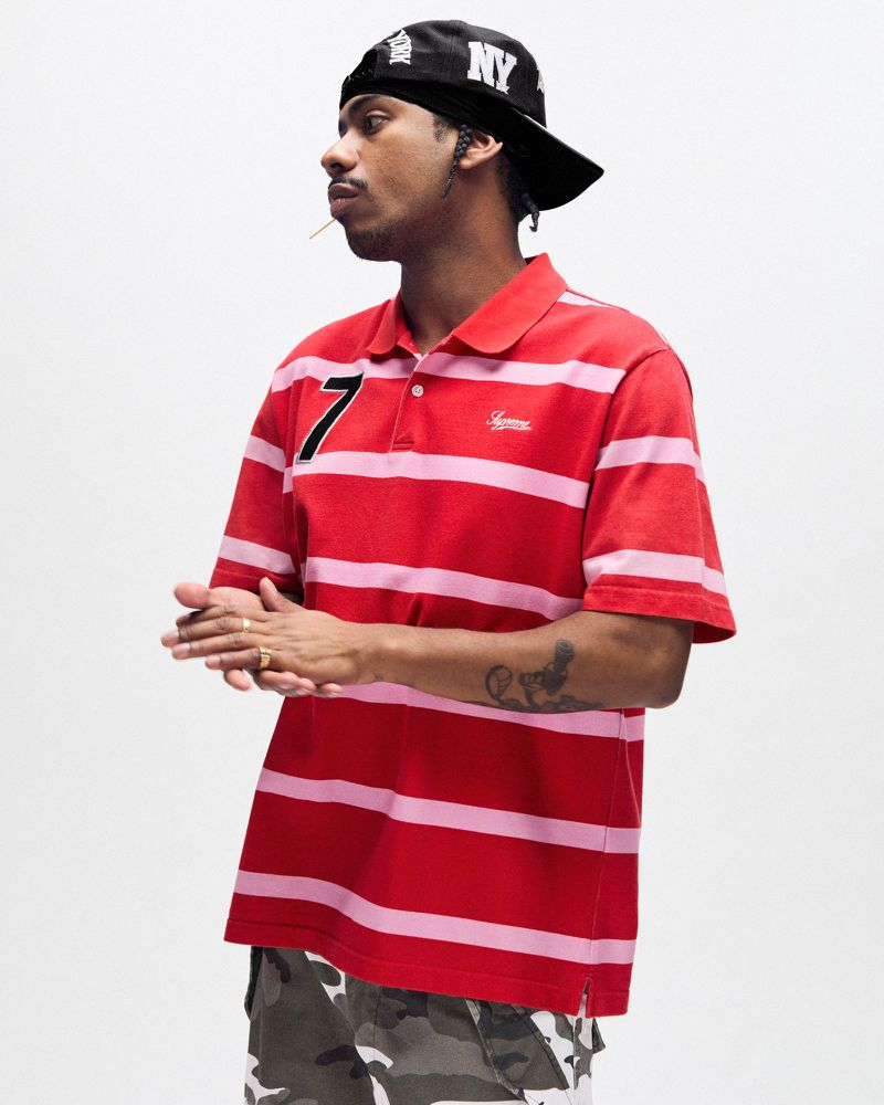 Portrait of African American man wearing striped polo shirt and baseball cap in a studio. He has a mustache and a goatee.