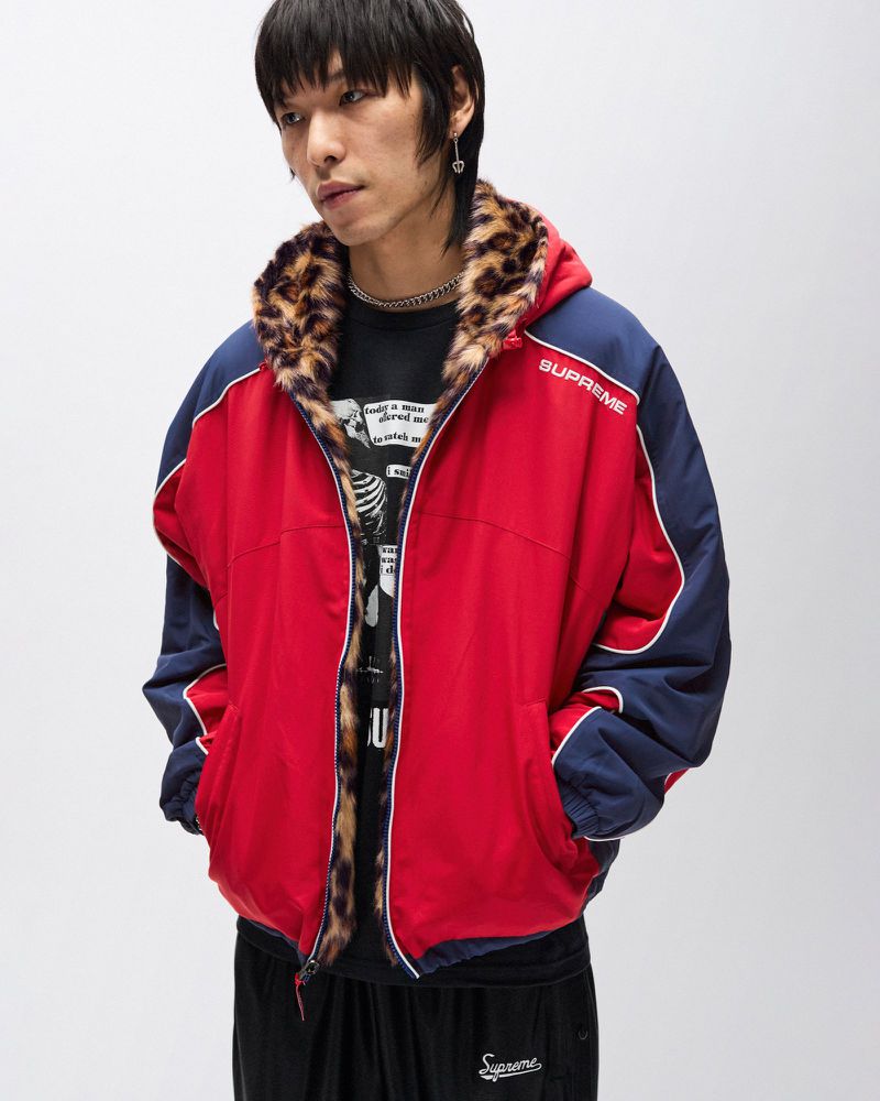 Asian male model in red and blue reversible jacket with leopard print trim, paired with black sweatpants in a neutral indoor setting.