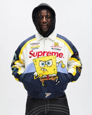 Adult male wearing a cream-colored racing jacket with Supreme and Spongebob Squarepants graphics in a studio setting with white background.