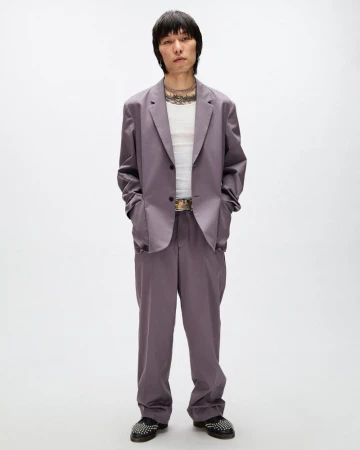 East Asian man standing in a relaxed mauve two-piece suit and white ribbed tank top against a plain white studio background.