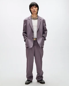 East Asian man standing in a relaxed mauve two-piece suit and white ribbed tank top against a plain white studio background.