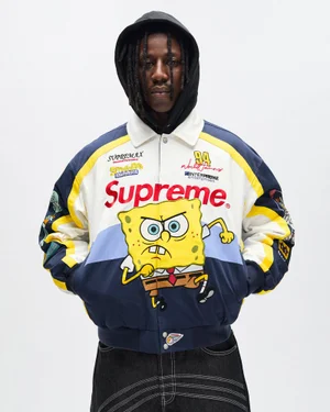 Man wearing black hoodie under a colorful Supreme Spongebob varsity jacket against a plain white background.