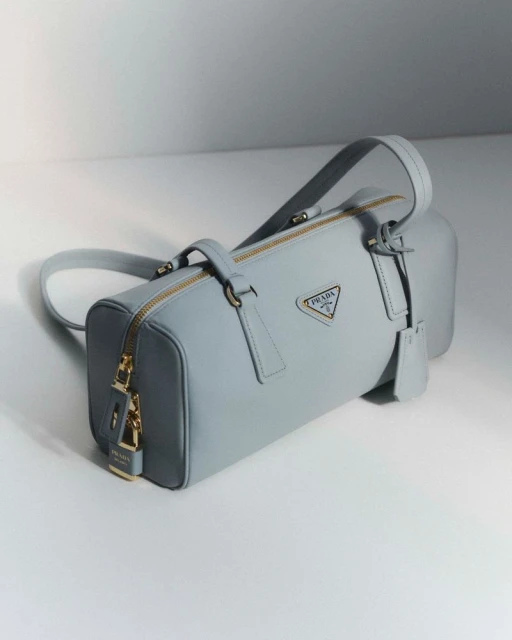 Light blue Prada bowling bag with gold hardware, including a padlock, studio lighting, and white background. Fashion photography.