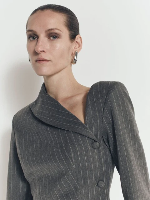 Woman poses in grey pinstripe blazer dress with metal hoop earrings against a white backdrop in a fashion photography shot.