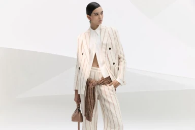 Model Meriam Turki wears a cream pinstripe suit with a brown knit tied at the waist against a geometric white backdrop.