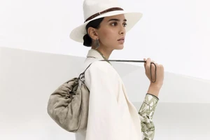 Model Meriam Turki wears a white wide-brim hat, cream jacket, and taupe suede shoulder bag for Brunello Cucinelli Lookbook S/S 2025.