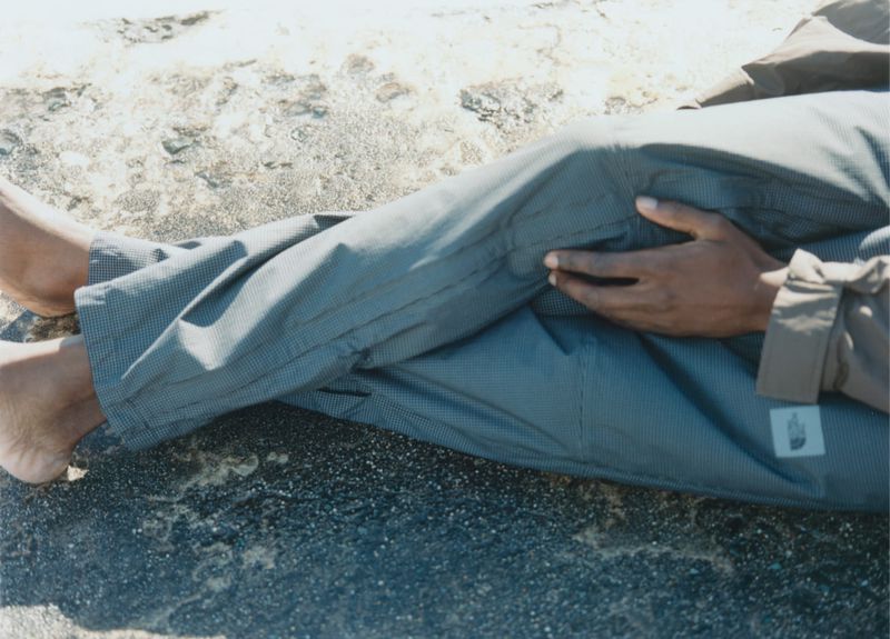 Person laying on a rock wearing pants and a jacket, with bare feet and hands visible. Outdoor shot with natural lighting.