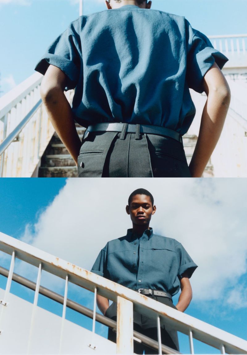 Two-shot fashion image of a Black male model in a blue shirt and black pants, standing on stairs under a blue sky with white clouds.