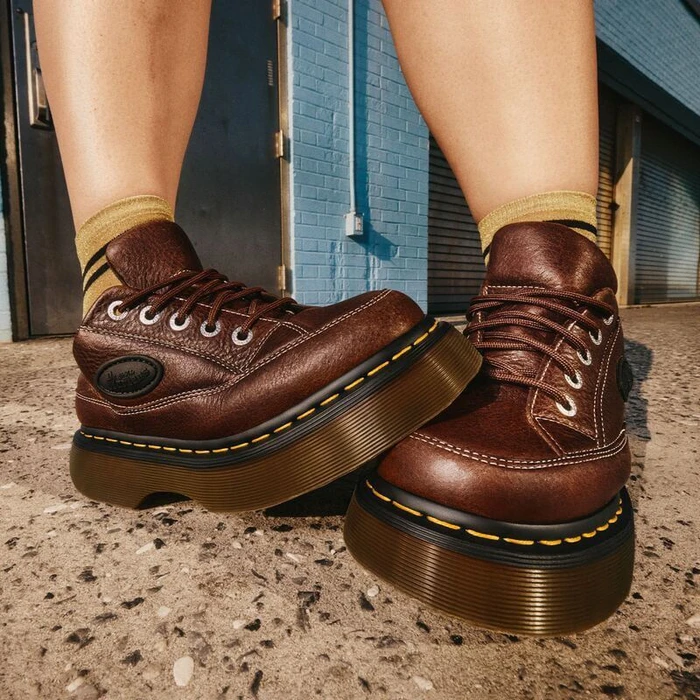 Close-up of brown leather Dr. Martens chunky platform shoes and striped ribbed socks standing on outdoor concrete pavement.