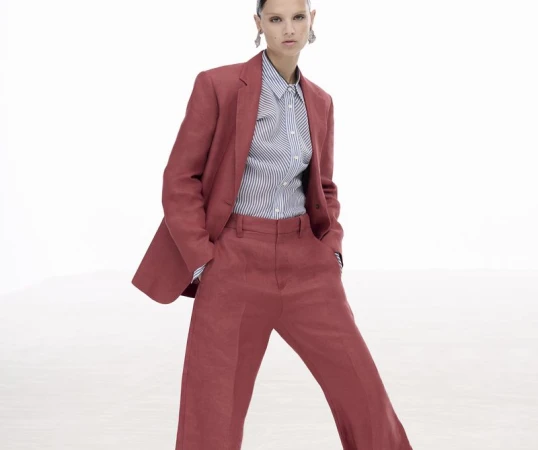 Model wearing a terracotta red suit and striped shirt against a plain white studio background.
