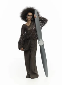 Model with voluminous hair wearing a textured v-neck sweater holding a large airplane propeller against a white background