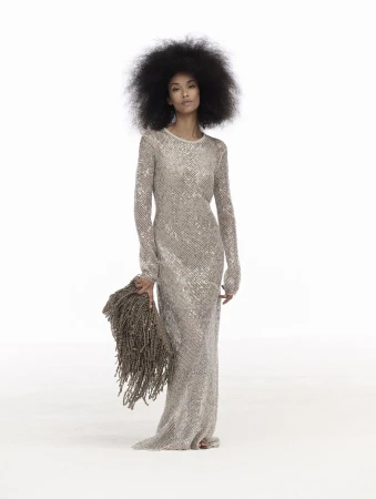 Model with voluminous dark hair wearing a long metallic silver gown against a plain white background